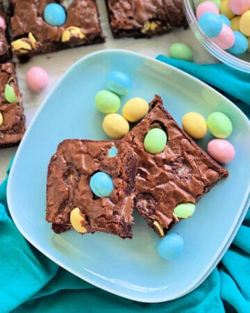Square photo of a blue plate with two brownies and colored eggs pressed in.