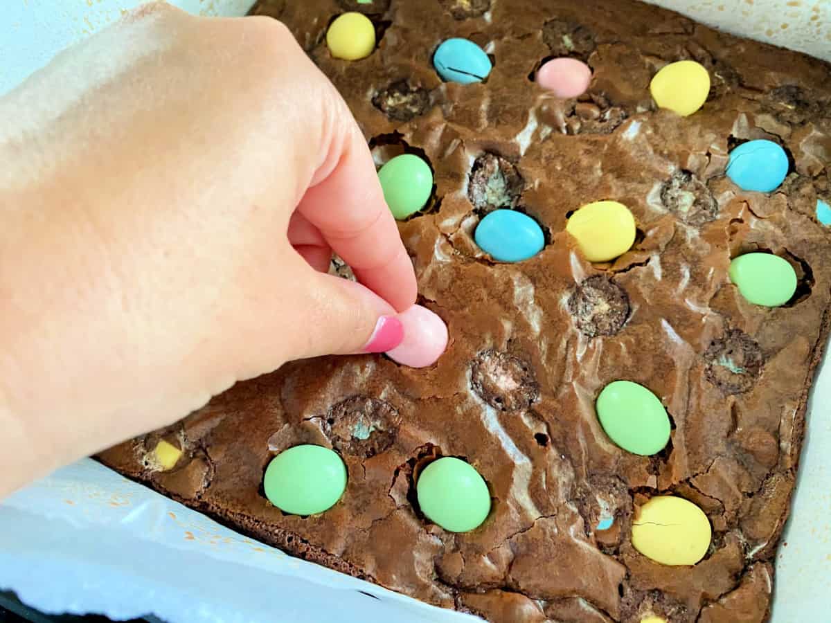 Female hand with pink nails placing a pink egg in the brownies.