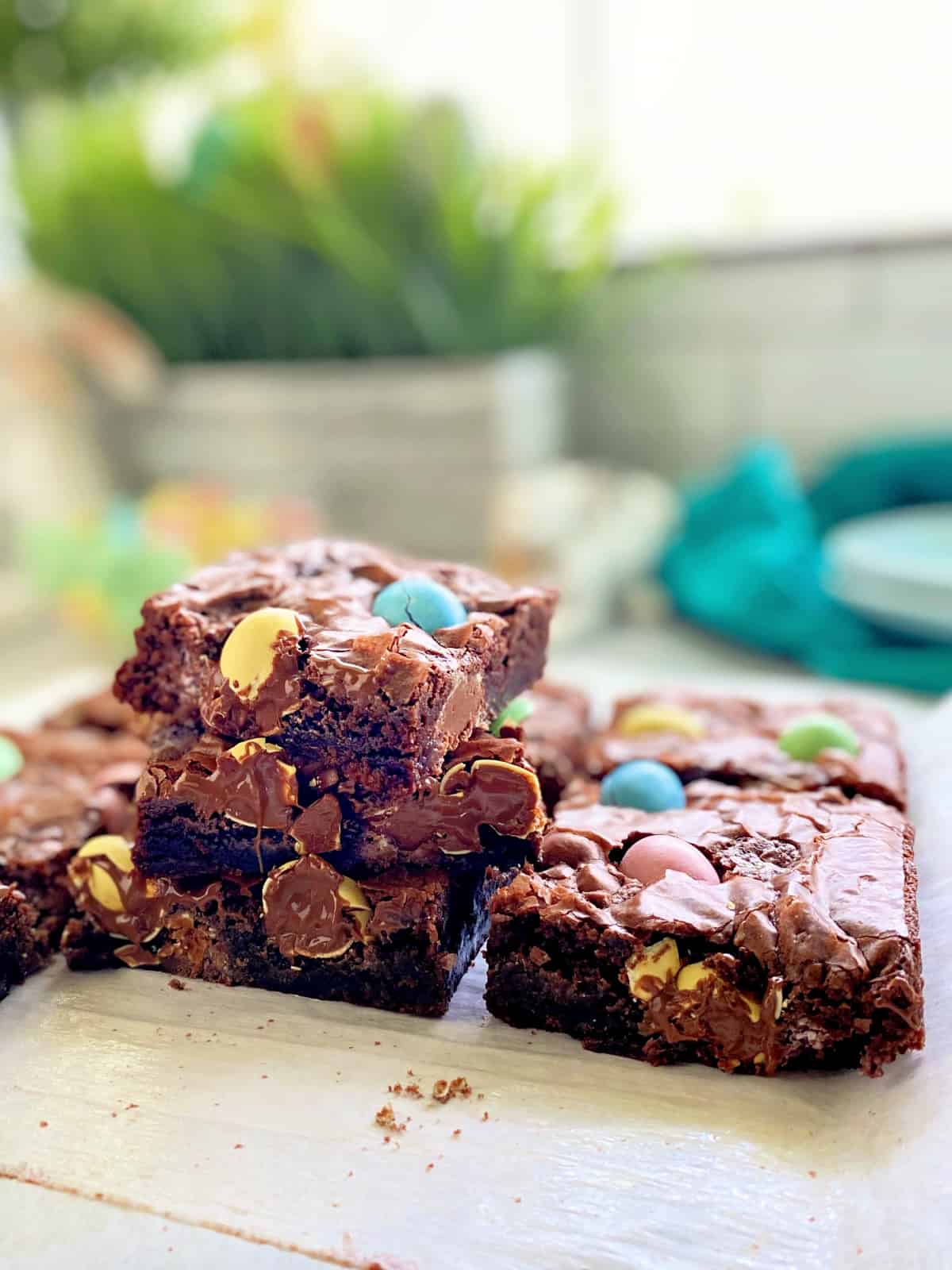 Three brownies stacked on top of each other sitting on white parchment paper.