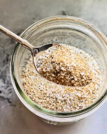 glass jar filled with seasoning and metal spoon taking a scoop out