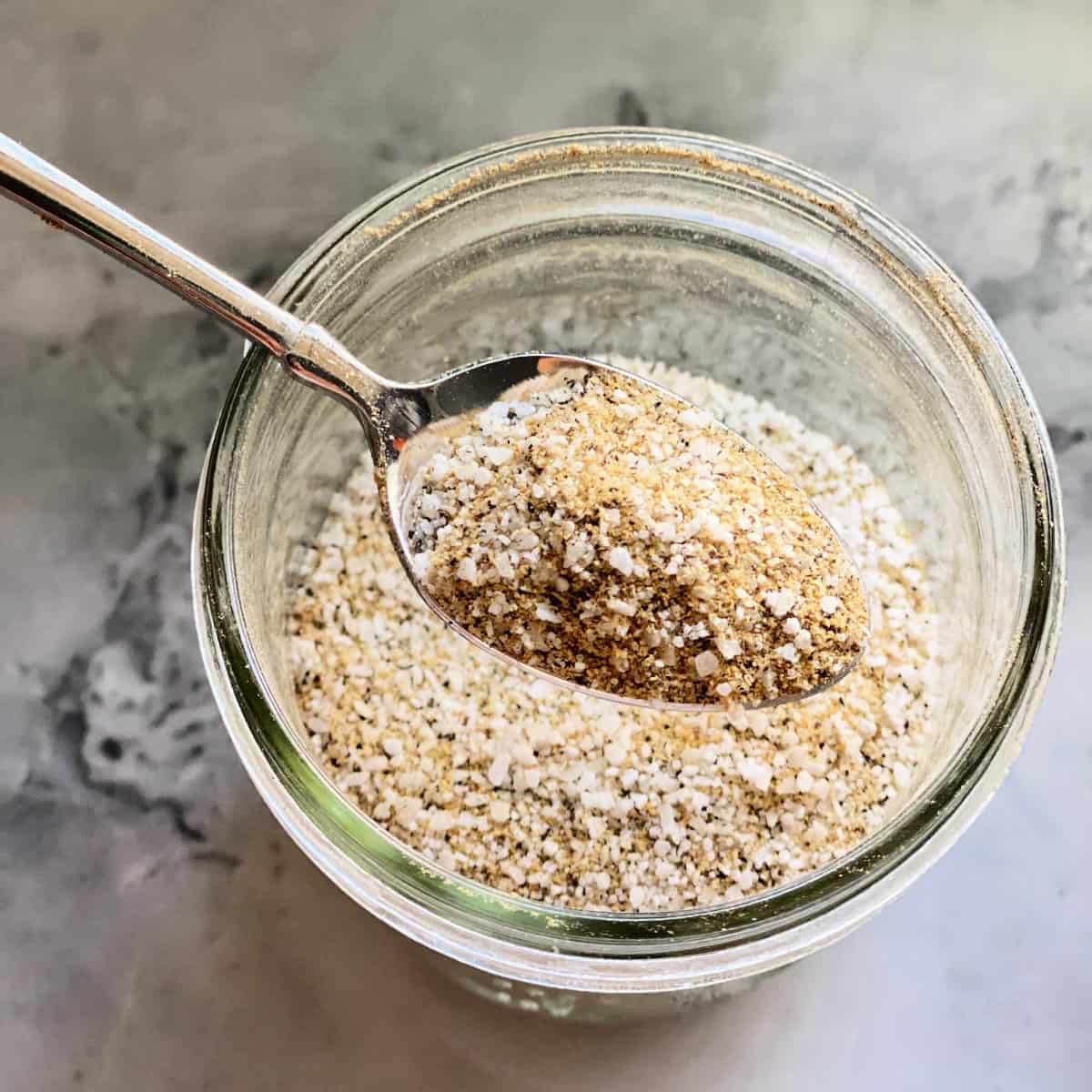 glass jar filled with seasoning and metal spoon taking a scoop out
