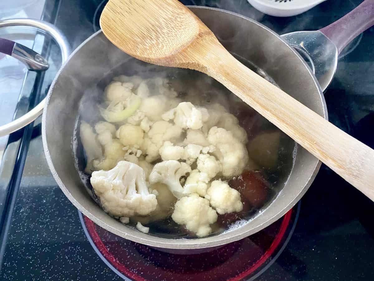 Cauliflower and potatoes boiling in a pot of water on the stove.