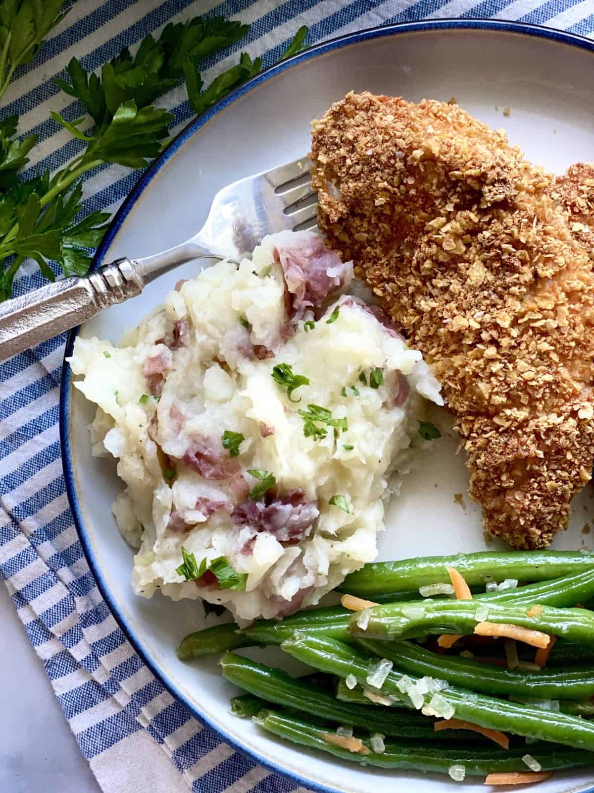 Potato and cauliflower mash on a white plate served with fried chicken and green beans