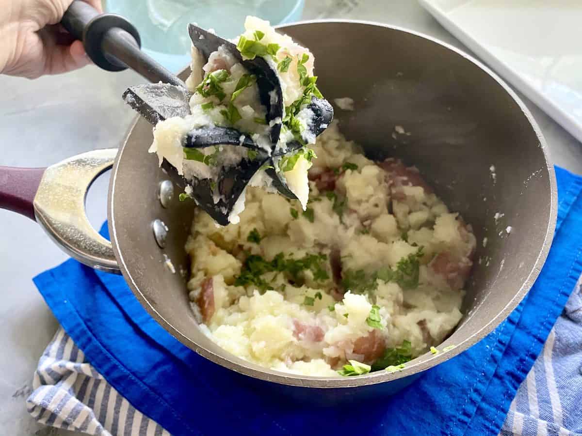 Potato and Cauliflower being bashed in a pot with parsley