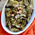 Seasoned Collard greens in a white oval serving dish over a red cloth