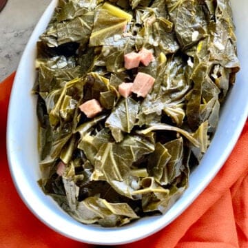 Seasoned Collard greens in a white oval serving dish over a red cloth