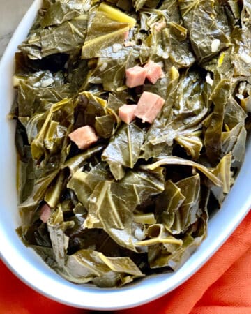 Seasoned Collard greens in a white oval serving dish over a red cloth