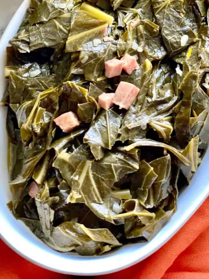 Seasoned Collard greens in a white oval serving dish over a red cloth