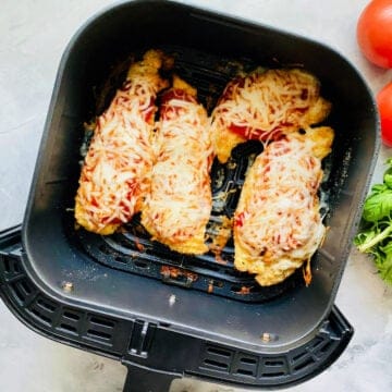 Top view of an air fryer drawer with four chicken breast.