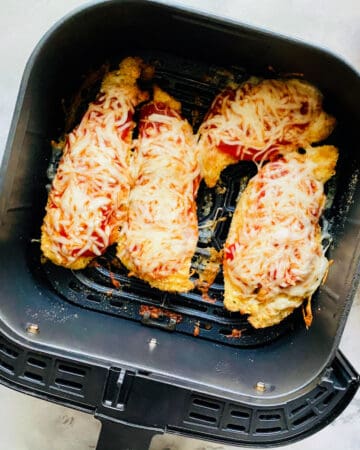 Top view of an air fryer drawer with four chicken breast.