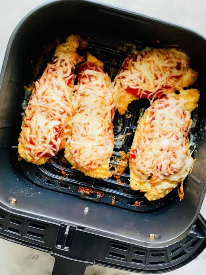 Top view of an air fryer drawer with four chicken breast.