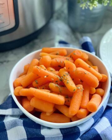 a white bowl filled with cooked baby carrots and a blue gingham cloth
