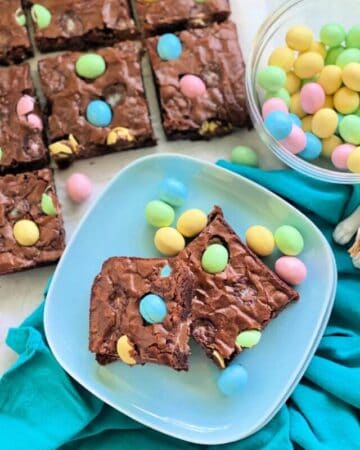 Two mini egg brownies on a blue plate with more brownies in the background