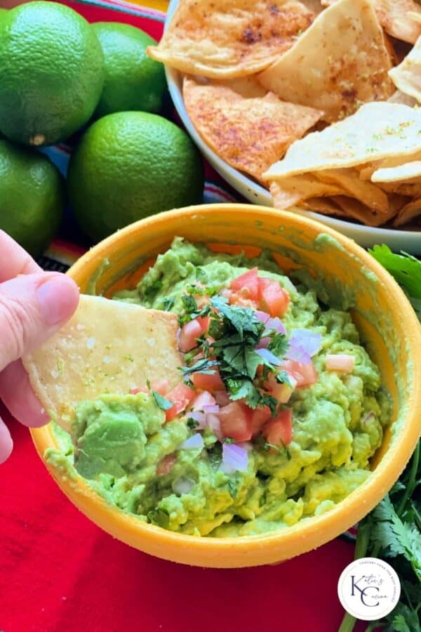 person's hand dipping a chip into a yellow bowl filled with guacamole