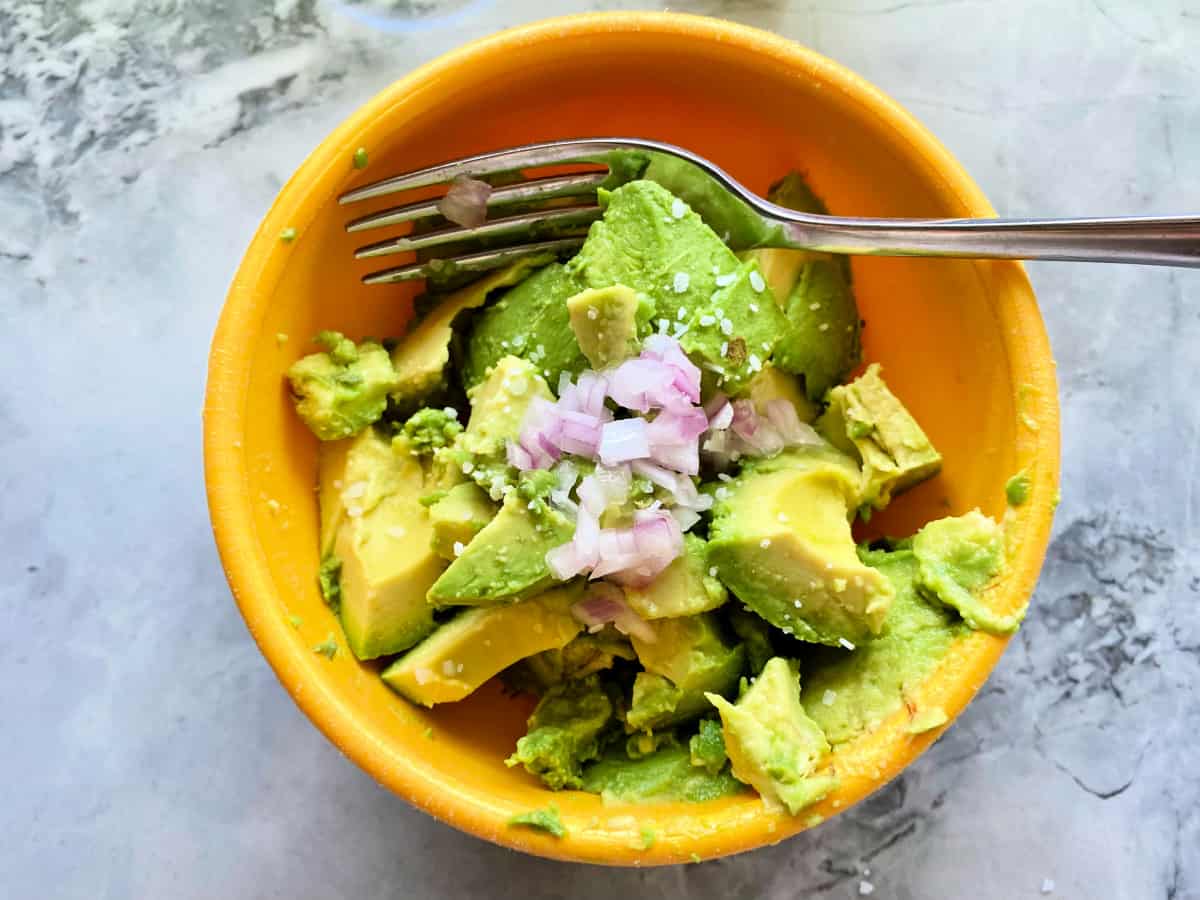 Yellow bowl with diced avocado and lime with a fork in the bowl.