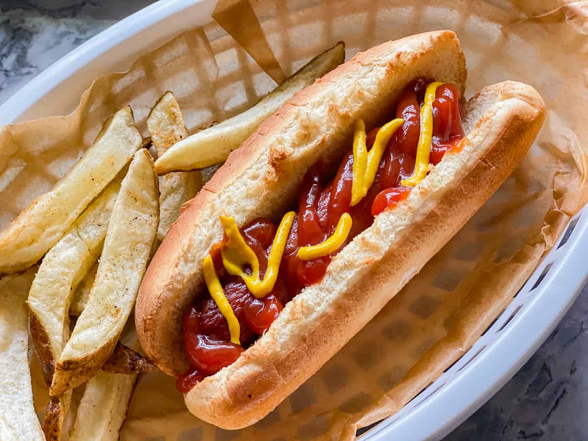 A hot dog in a basket lined with paper and a side of fries.