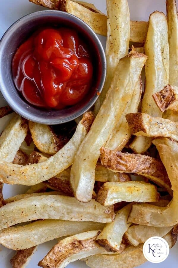 white glass place with French fries and a silver dipping cut filled with ketchup.