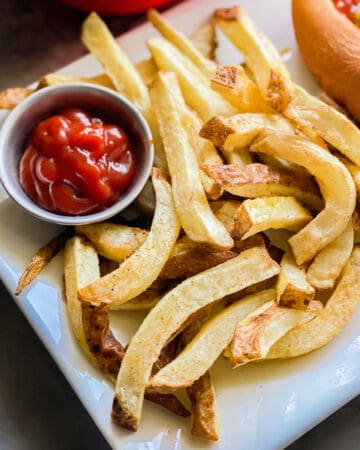 French fries on a white platter with with a small bowl of ketchup next to it.