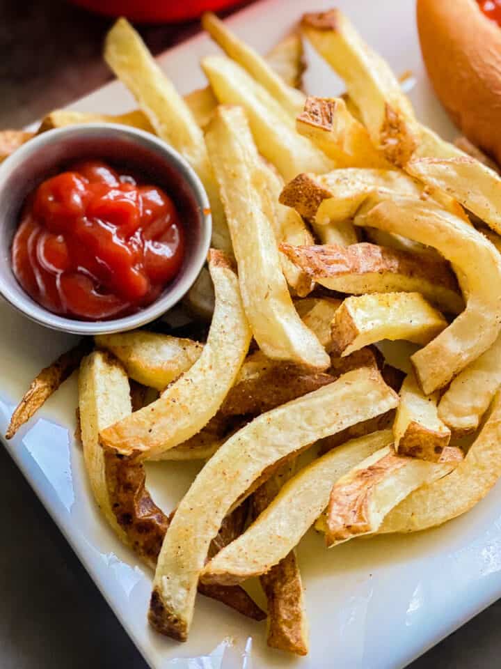 French fries on a white platter with with a small bowl of ketchup next to it.