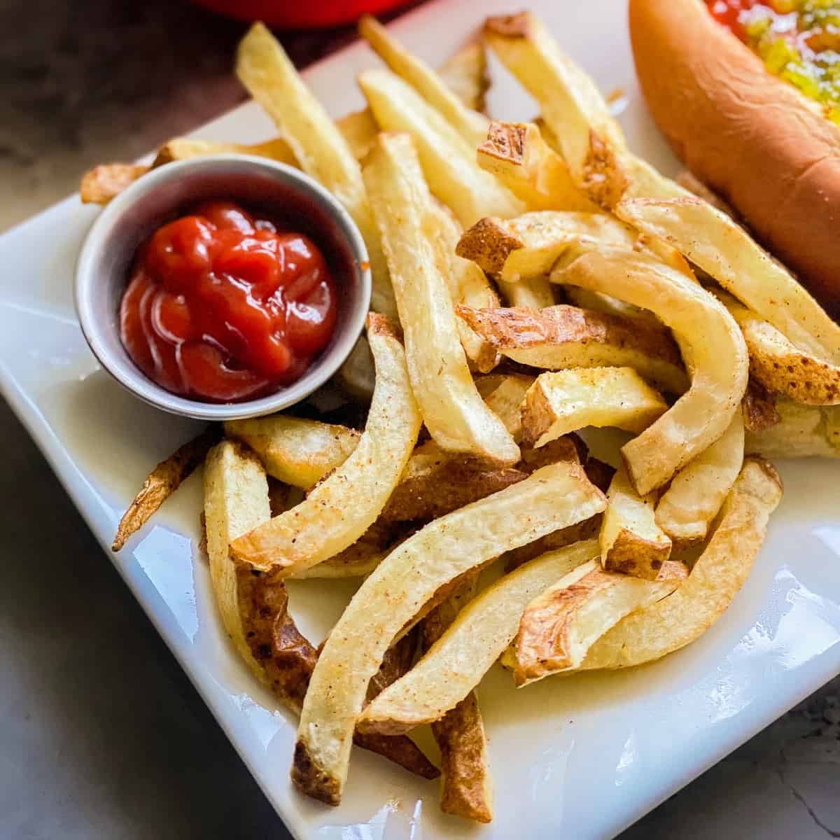 French fries on a white platter with with a small bowl of ketchup next to it.