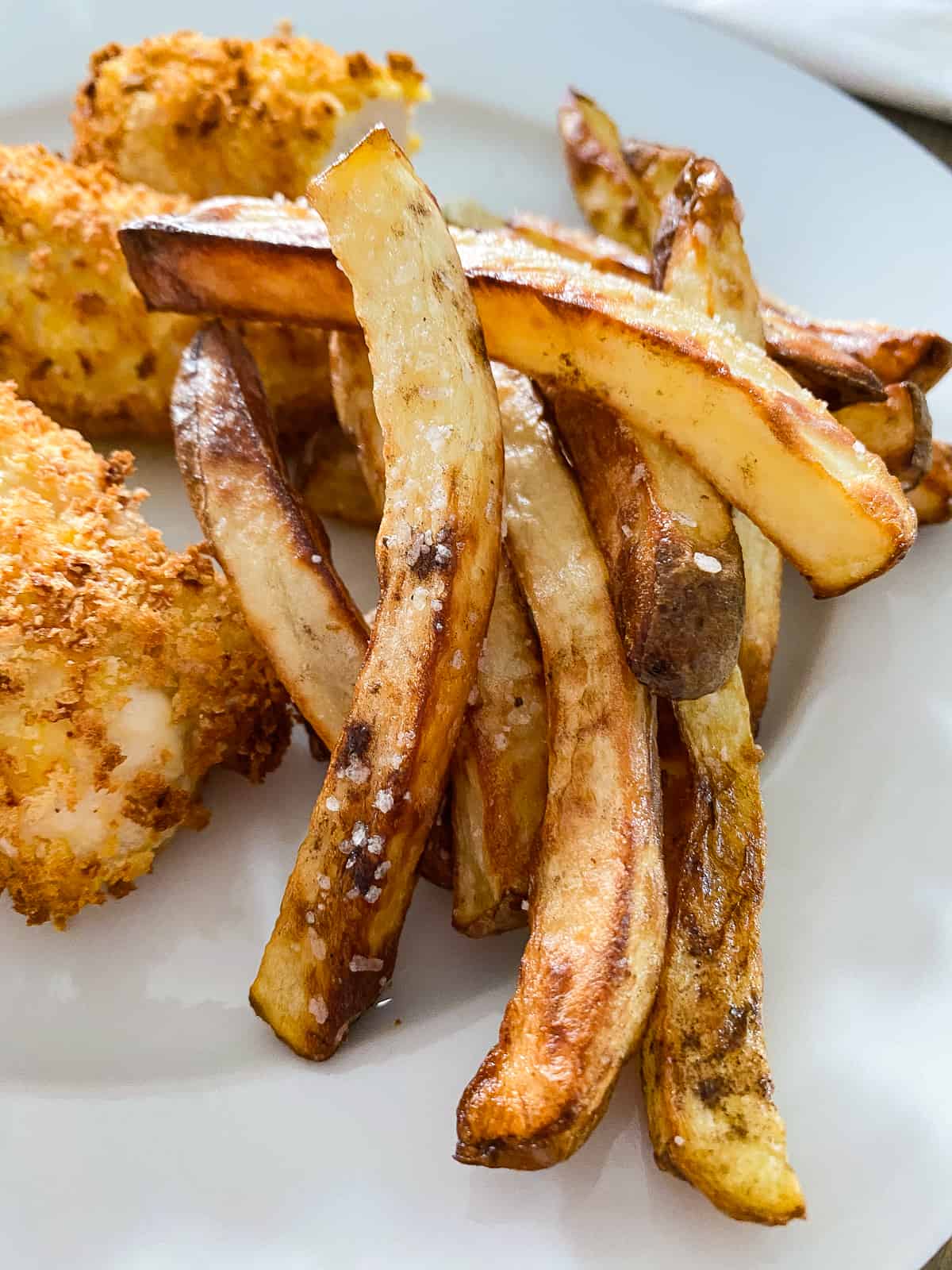 White plate with French fries with salt flakes with chicken tenders in the background