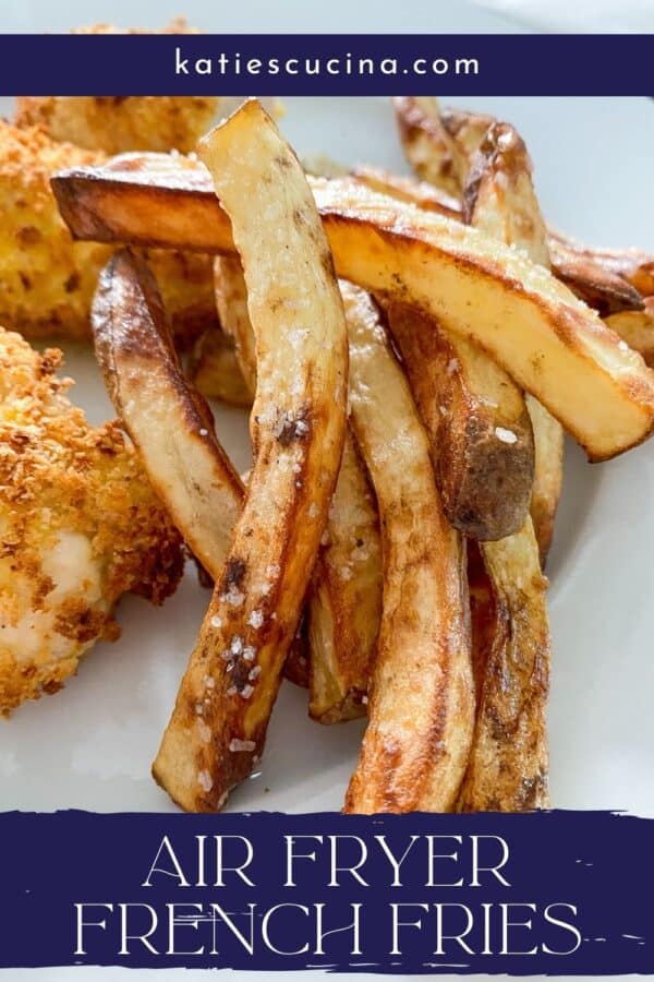 White plate with French fries with salt flakes with chicken tenders in the background with recipe title text on image for Pinterest.