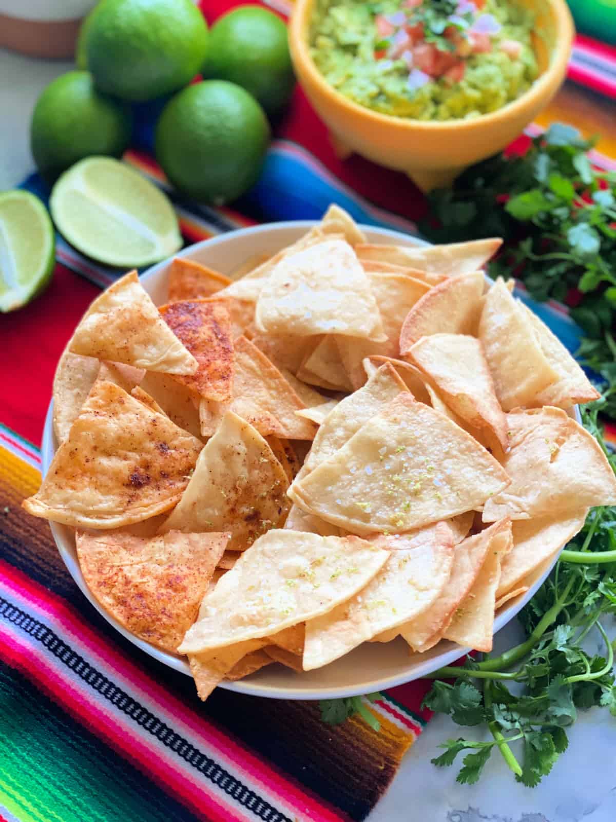 White bowl filled with corn tortilla chips with guac and limes in the background.