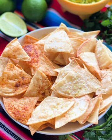 White bowl filled with corn tortilla chips with cilantro and dip in background.