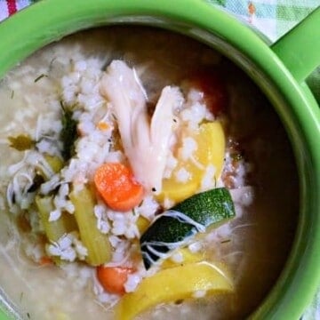 Green bowl filled with chicken soup and various vegetables