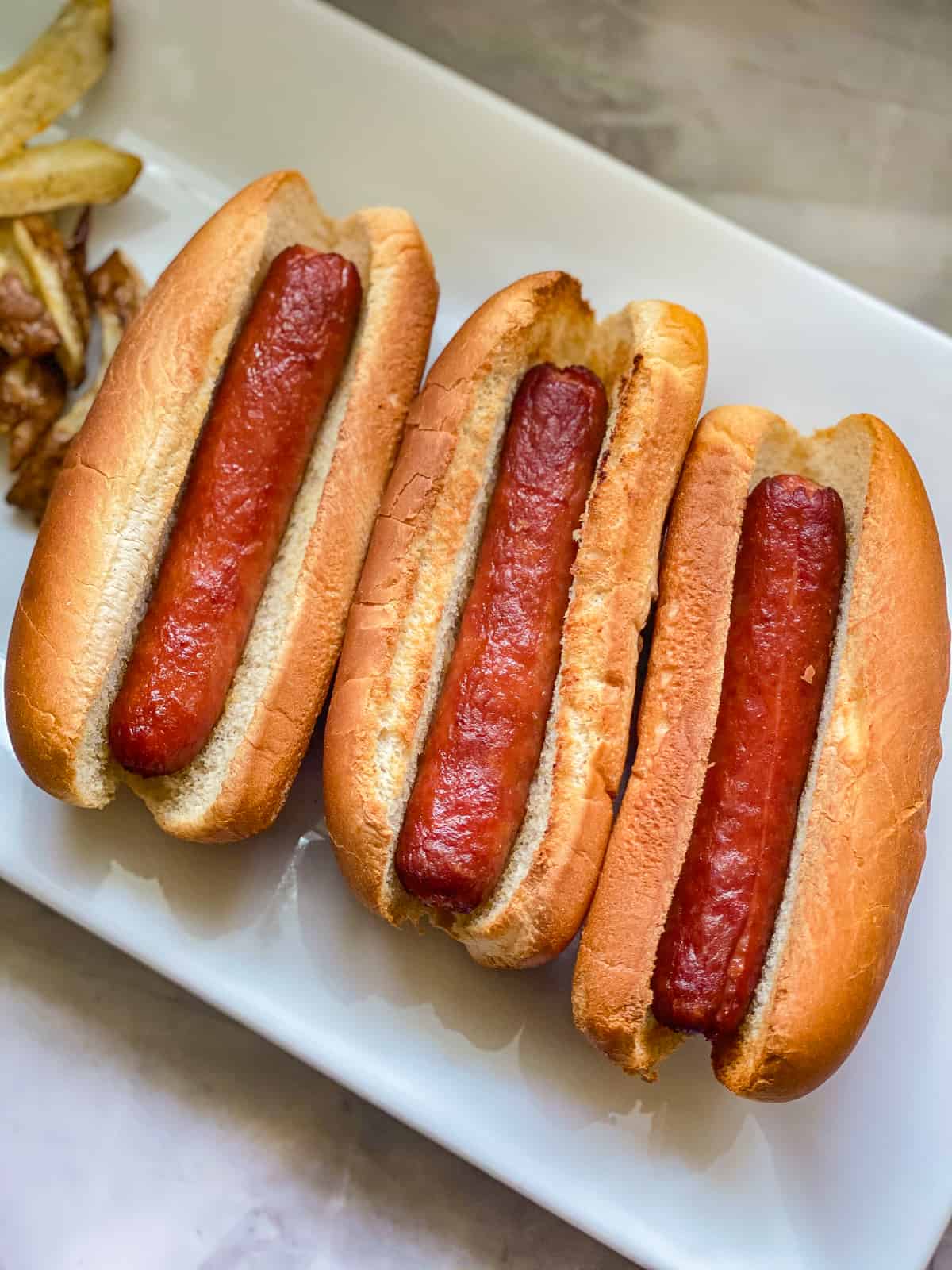 Three hot dogs on a white platter.