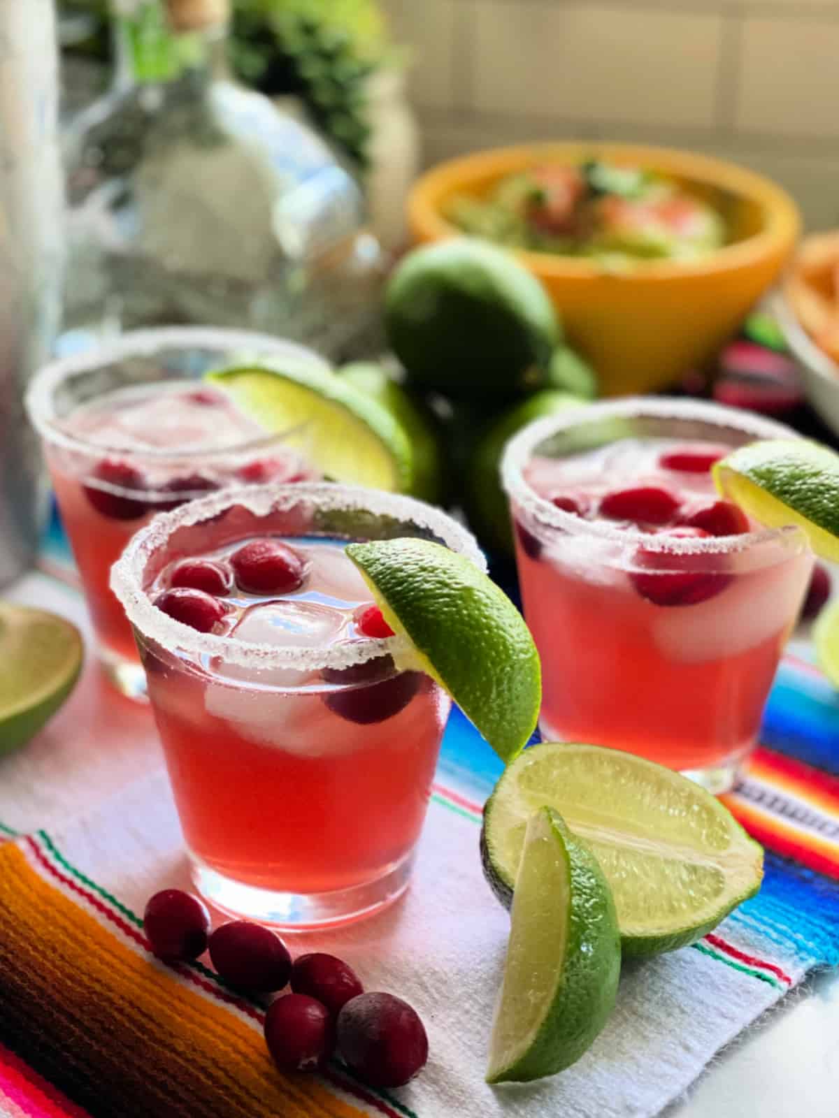 Three glasses with pink drink, cranberries, and ice with lime wedges.