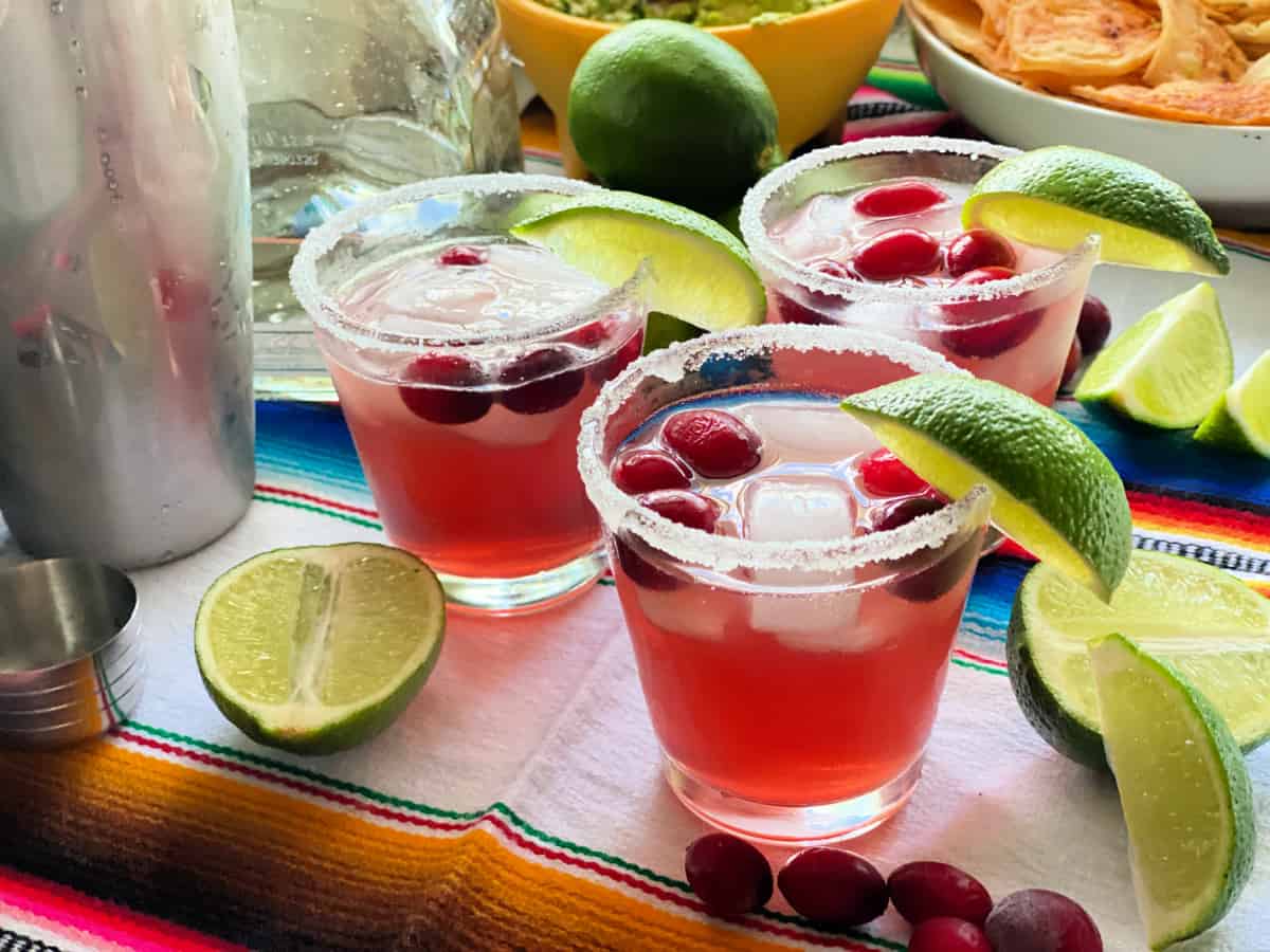 Three glsases with pink margarita with sugar rim with lime wedge.