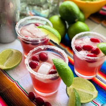 three glasses with cranberries, sugar, lime wedges.