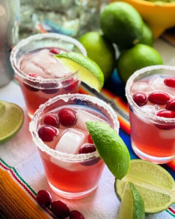 three glasses with cranberries, sugar, lime wedges.