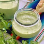 Small glass jar with green sauce with cilantro next to it.