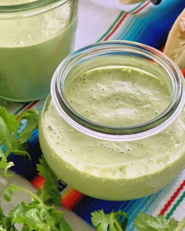 Small glass jar with green sauce with cilantro next to it.