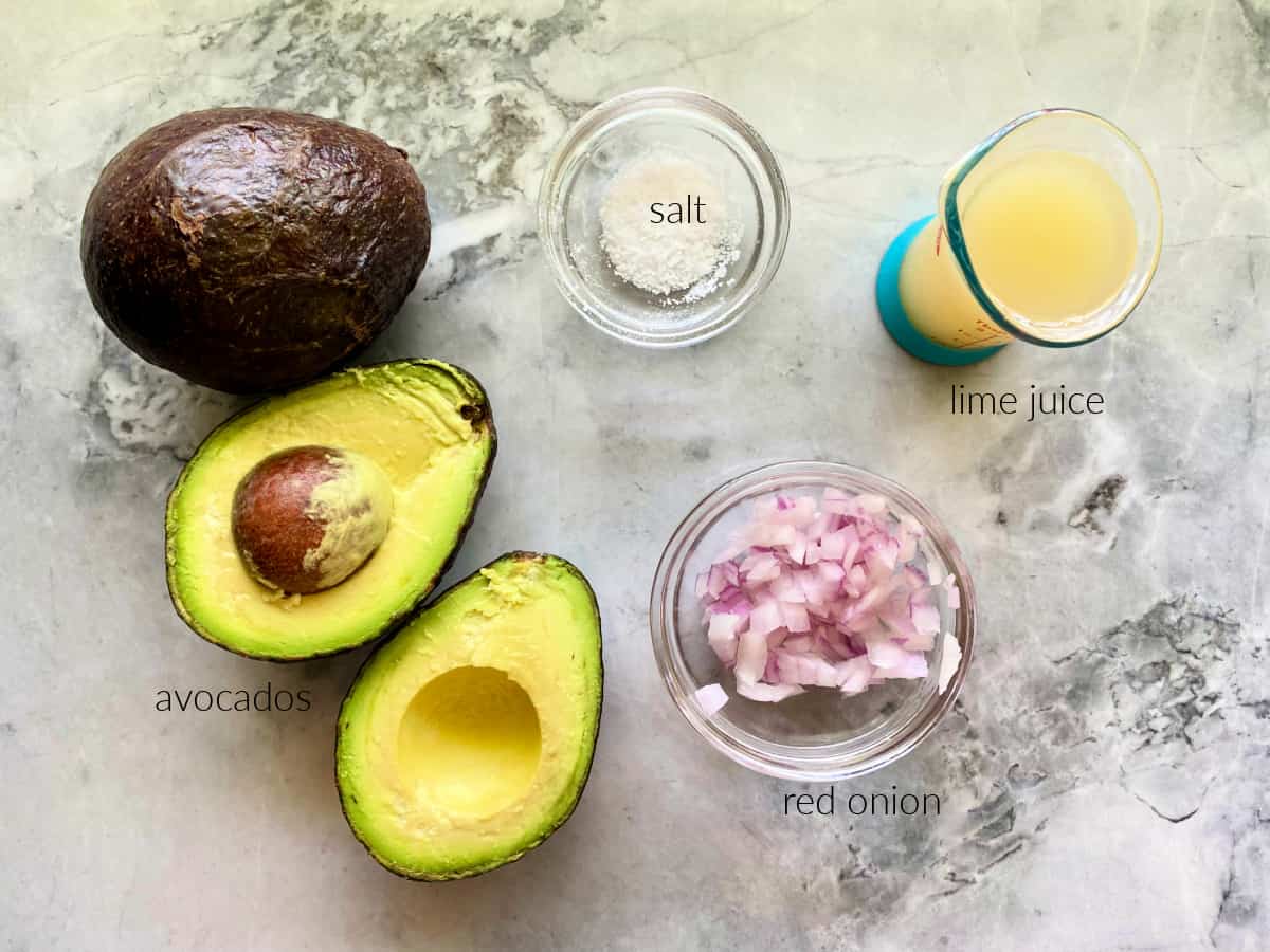 Ingredients on counter; avocados, chopped red onion, salt, and lime juice. 