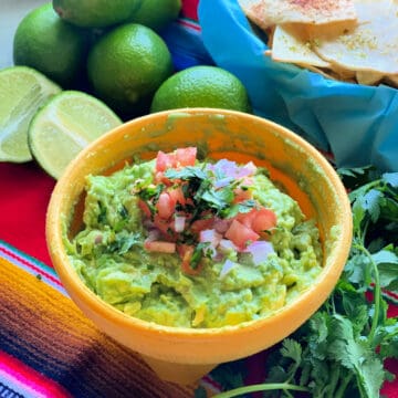 a yellow bowl filled with guacamole with diced tomato and onion on top