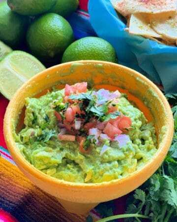 a yellow bowl filled with guacamole with diced tomato and onion on top