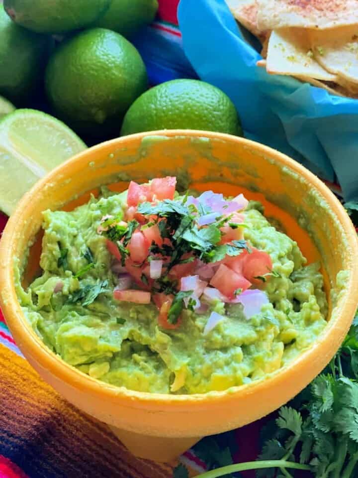 a yellow bowl filled with guacamole with diced tomato and onion on top