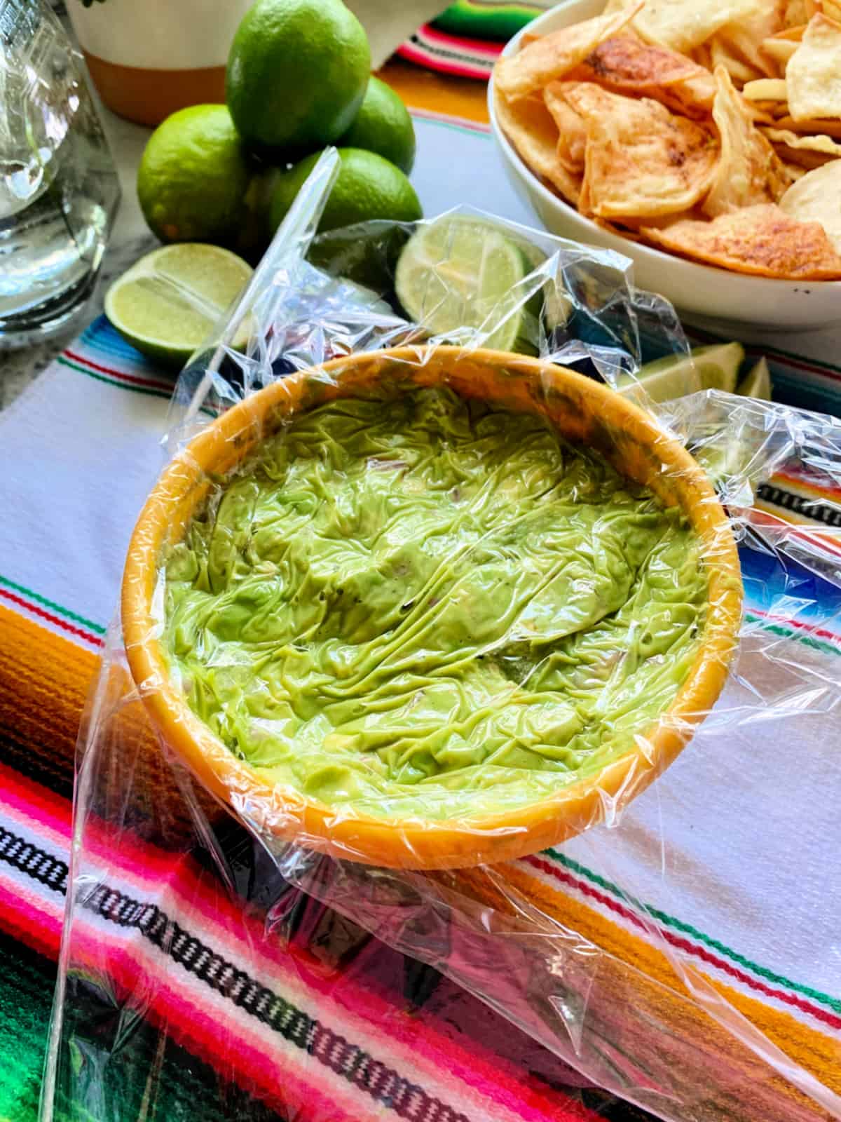 Yellow bowl filled with guacamole and plastic wrap.  