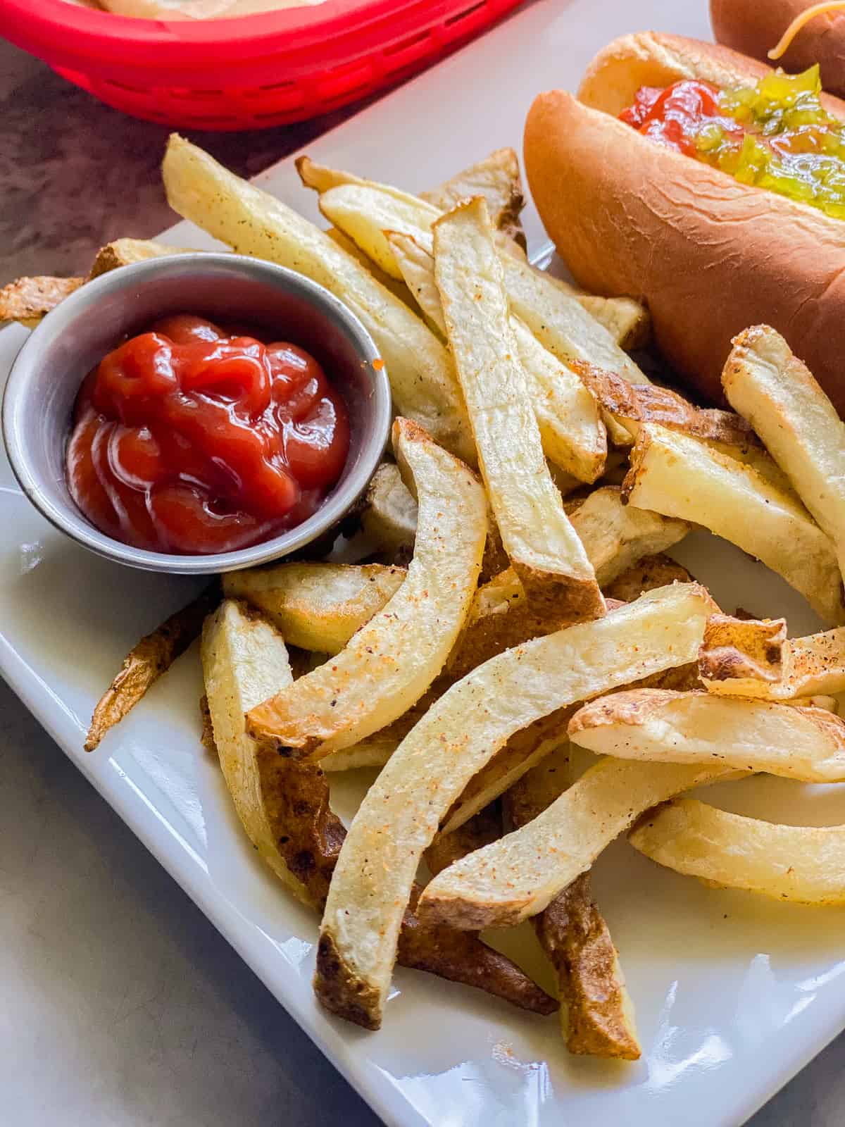 French fries on a white plate with a silver dipping cup of ketchup