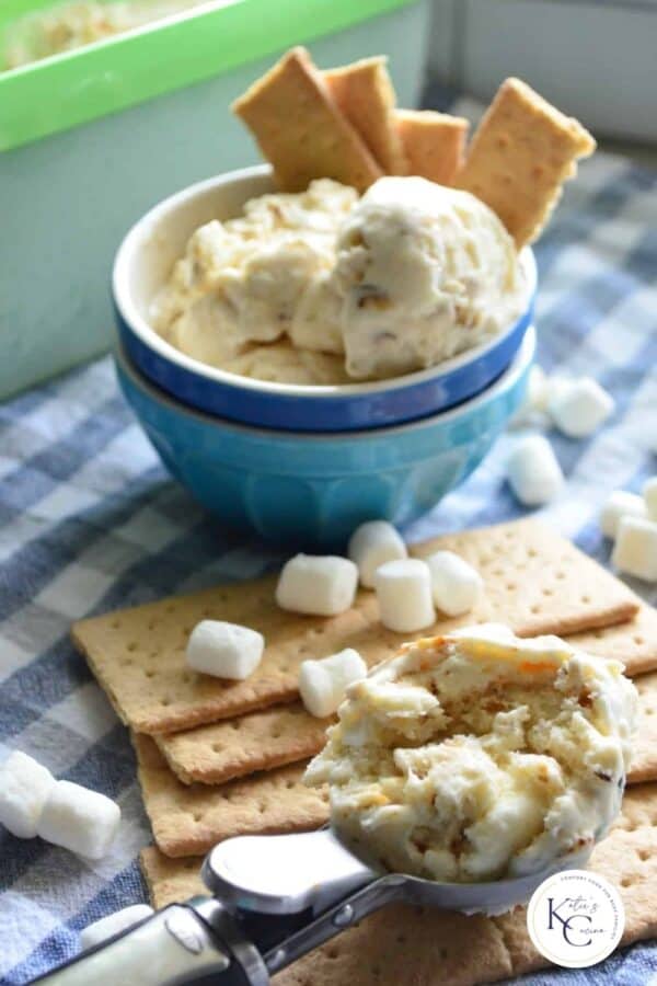 Ice cream scoop with ice cream resting on top of graham crackers and mini marshmallows with logo on right corner.