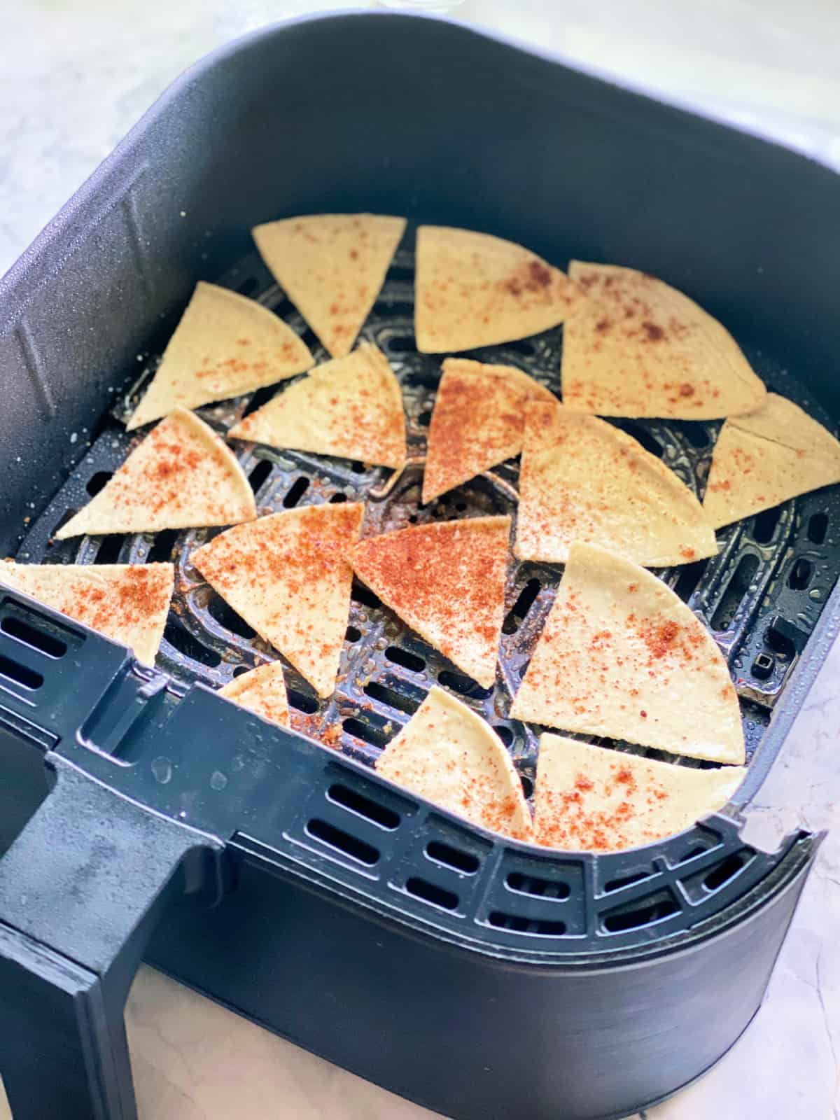 Black basket filled with corn tortilla chips with seasoning on top.