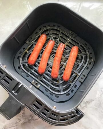 black air fryer on white marble counter with four cooked hotdogs inside