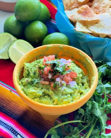 A yellow bowl of guacamole topped with diced tomato and onion
