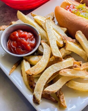 French fries on a white plate with a silver dipping cup of ketchup
