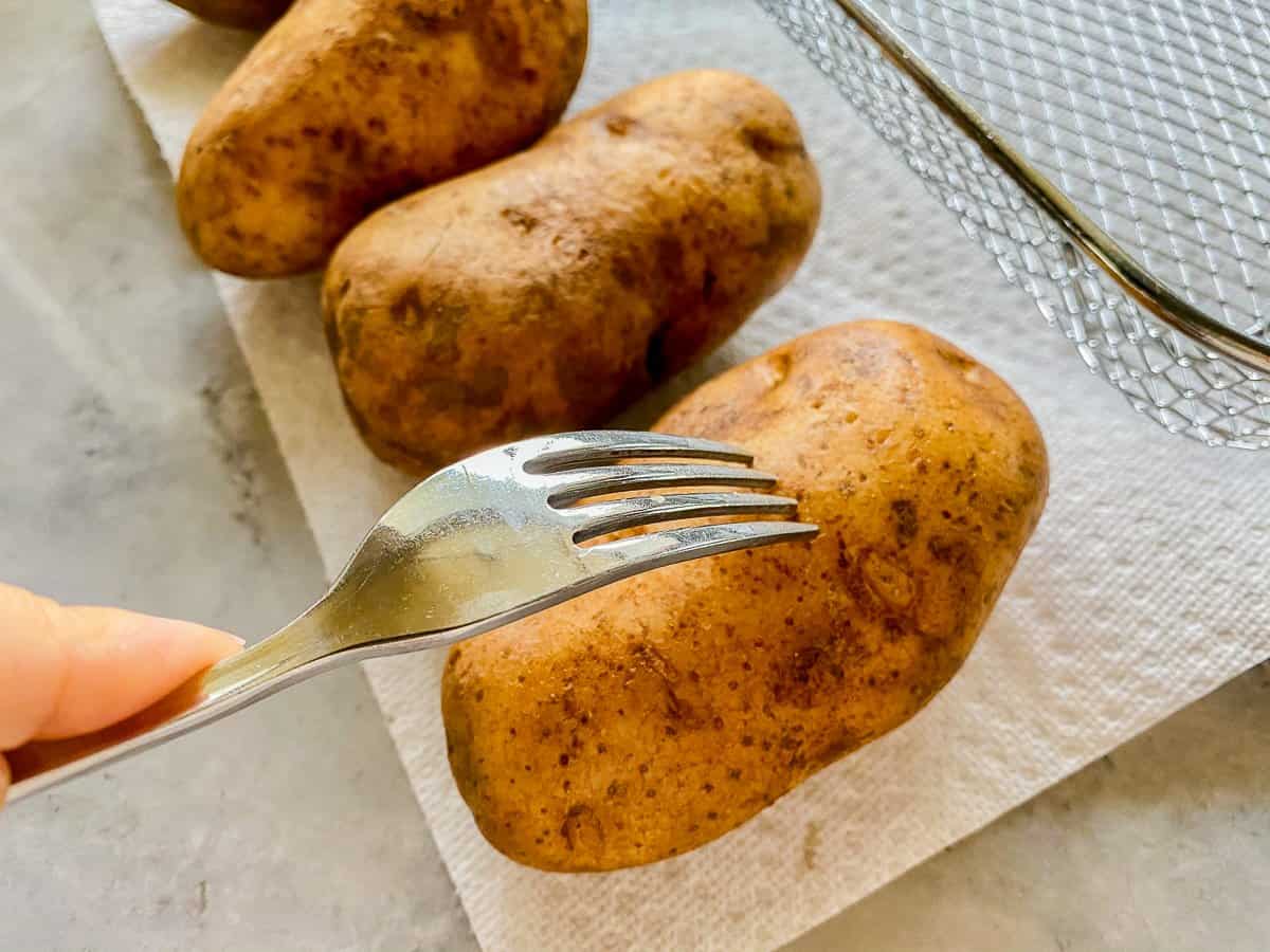 3 potatoes on a white paper towel. the first potato has a fork in it.