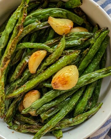 White bowl of green beans with garlic divided up close.