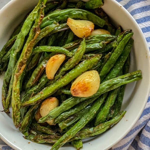 White bowl of green beans with garlic divided up close.